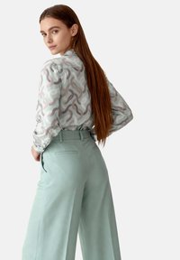 Light-patterned, long-sleeved blouse in pastel colors, paired with high-waisted, wide-leg trousers in mint green. Smooth texture, tailored fit.