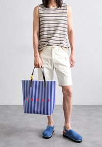 Bluzka bez rękawów w paski, kremowe szorty, torba typu tote w niebiesko-fioletowe paski z czerwonym napisem "MARNI", niebieskie klapki wsuwane z czarną podeszwą.