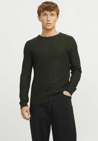 Dunkelgrüner Strickpullover mit strukturiertem Design, langen Ärmeln und Rundhalsausschnitt, kombiniert mit schwarzen Hosen.