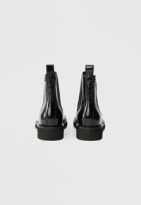 Botines de charol negro con un acabado suave, paneles laterales elásticos y una suela de goma apilada. Diseño minimalista con sutiles detalles de costura.