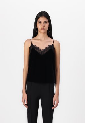 Svart fløyels camisole med blonder langs utkanten av halslinjen, tynne justerbare stropper og en avslappet passform. Kombinert med svarte tettsittende bukser.