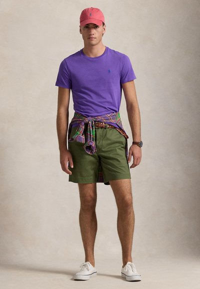 Fialové tričko, olivovo zelené šortky a ružová šiltovka. Kockovaná košeľa zviazaná v páse. Biele tenisky dotvárajú ležérny vzhľad.