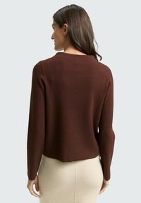 Pull en tricot brun avec un col rond, des manches longues et un ourlet légèrement court, associé à une jupe beige ajustée.