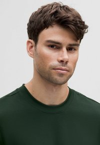 Tamsiai žalia crewneck tipo marškinėliai, pagaminti iš minkštos medžiagos, pasižymintys lygiu paviršiumi ir subtiliomis siuvinėjimo detalėmis ant pečių.