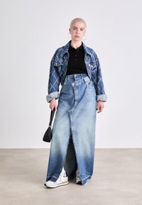 Džínová bunda s diamantovým vzorem přes černé polo tričko, spárovaná s dlouhou, vyblitou džínovou sukní s předním rozparkem a bílými teniskami.