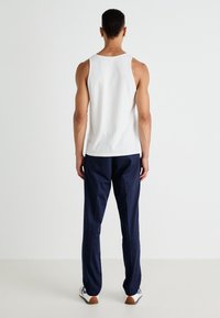 Débardeur en coton blanc assorti à un pantalon bleu marine, avec une texture lisse et une coupe ample. Les chaussures sont blanches avec des accents bleu marine et des semelles marron.