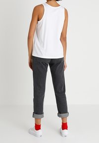 Hvid ærmeløs top, mørkegrå jeans med opsmøring, røde sokker og hvide sneakers. Simpelt design, letvægtigt stof, afslappet pasform.