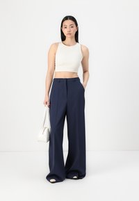 Calças largas navy com pregas frontais, combinadas com um top cropped ajustado em creme. Os acessórios incluem uma pequena mala de ombro branca.