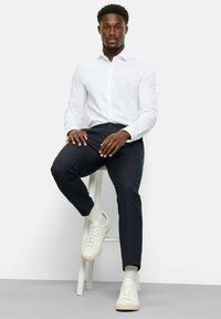 Weißes Hemd mit Knopfleiste, dunkle Hose und weiße Sneakers. Einfaches Design, taillierte Form, glatte Textur, mit dezenten Akzenten und klaren Linien.