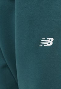 Τζόγκερ αθλητικά σε τιρκουάζ χρώμα με απαλό υλικό και κεντημένο λευκό λογότυπο "NB" στο πλάι. Απλός, λιτός σχεδιασμός.