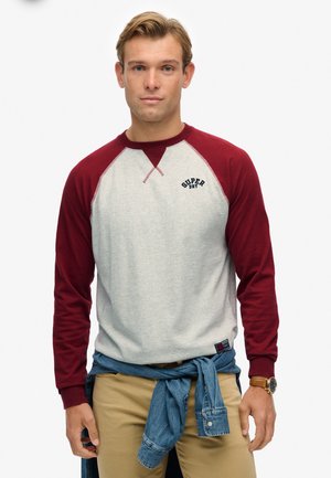 Grijze en bordeauxrode sweatshirt met lange mouwen en raglanmouwen, "SUPER DRY" logo op de borst en een spijkerhemd om de taille geknoopt.