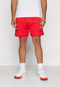 Red mesh athletic shorts with black "BULL" logo, paired with white sneakers featuring red accents and textured soles, topped with a white shirt.