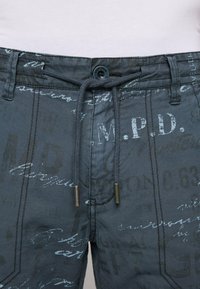 Šedé šortky se stahovací šňůrkou a knoflíkem, zdobené texturovaným vzorem písmen a čísel v světlejších odstínech.