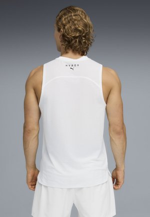 Man met krullend haar die een wit mouwloos sportshirt draagt met het merk "HYROX" en het Puma-logo, en witte korte broek, gezien van achteren.