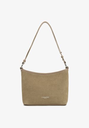 Sac à main en suède beige avec un design courbé et une longue bandoulière. Présente des accessoires en métal argenté et un logo en bas.
