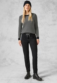 Svart tröja med vita prickar, svarta joggerbyxor med dragsko i midjan och svarta snörstövlar. Strukturerad stickning och avslappnad passform.