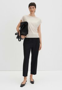 Top corto beige a maniche corte, pantaloni neri su misura, ballerine nere a punta quadrata e una grande borsa a rete nera. Tessuto liscio e design strutturato.
