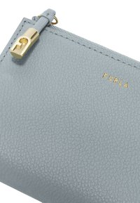 Lichtgrijze, gestructureerde leren ritspouch met gouden hardware en merklogo, voorzien van een soepele ritstreker en zichtbare stikdetails.