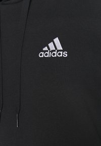 Sudadera negra con tejido texturizado, que presenta un logotipo de Adidas bordado en plata en el pecho y detalles a juego en los cordones.