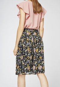 Bloemrijke rok met een zwarte basis, voorzien van grote roze, blauwe en groene bloemen. Gecombineerd met een lichtroze blouse met ruches aan de mouwen.