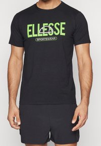 Černé bavlněné tričko s velkým zeleným logem "ELLESSE" a textem "SPORTSWEAR", krátké rukávy a klasický kulatý výstřih.