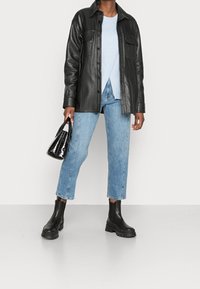 Veste en cuir noir, pull bleu clair, jean bleu clair, bottines noires à semelles épaisses, et petit sac à main en cuir verni.