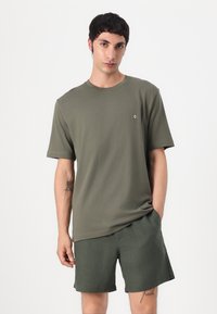 Olivegrünes Baumwoll-T-Shirt mit kurzen Ärmeln, Rundhalsausschnitt und kleinem Logodetail, kombiniert mit passenden olivegrünen Shorts. Schlichtes, lässiges Design.