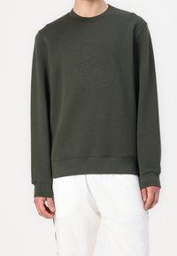 Sweat-shirt vert olive avec un col rond et des poignets côtelés. Un logo embossé ton sur ton est centré sur le devant.