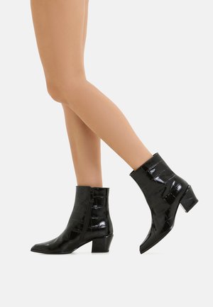 Schwarze Lackleder-Ankle Boots mit Krokodilstruktur, dreieckiger Spitze und einem niedrigen Blockabsatz. Reißverschlussdetail auf der Außenseite.