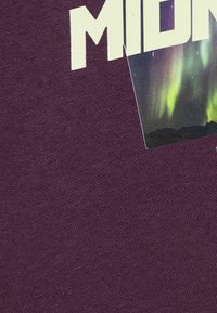 Lila bomullstyg med en textur som visar synliga fibrer. Innehåller en vit text "MIDNIGHT" och en liten bild av norrskenet.