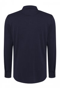 Camisa de manga larga de color azul marino, hecha de una tela suave, que cuenta con un cuello tipo polo, puños abotonados y un dobladillo curvado para una silueta alargada.