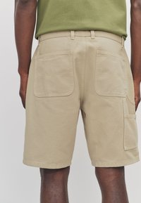 Beige cargo shorts with two large back pockets, stitched detailing, and a straight cut. Made from durable fabric, featuring a standard waistband.