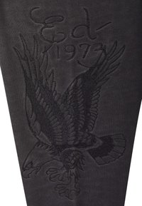 Tela negra con un diseño bordado de un águila, que presenta un detallado intrincado y el texto "Águila 1973". La textura es suave y lisa.