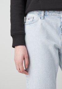 Světlé modré džíny s rovnými nohavicemi a jemným efektem opotřebení, doplněné černou žebrovanou mikinou.