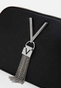 Black textured bag featuring a silver metal "V" emblem with a chain tassel attachment. Smooth finish with rounded edges.
