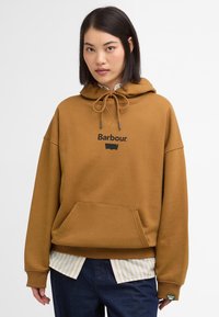 Καφέ φούτερ με κορδόνι, καγκουρό τσέπη και μαύρο λογότυπο "Barbour". Φορεμένο πάνω από μια ριγέ μπλούζα με πράσινη ετικέτα.