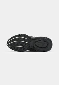 Suela de zapatilla negra con agarre de goma texturizada, que presenta patrones de relieve pronunciados y detalles de marca en relieve, diseñados principalmente para ofrecer tracción.