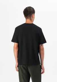 Camiseta negra de cuello redondo con mangas cortas, hecha de un tejido suave. Presenta un corte recto y un pequeño detalle del logo en el costado.