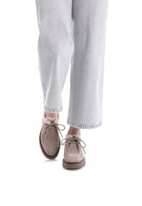 Zapatos de ante beige con forro de piel y diseño de cordones, suela gruesa, usados con pantalones de mezclilla sueltos de color gris claro.