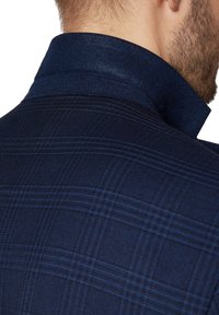 Marynarski plaidowy żakiet z teksturowanej tkaniny, wyraźnym kołnierzem, delikatnymi niebieskimi liniami oraz zorganizowanym krojem. Teksturowane plecy z dopasowanym krojem.