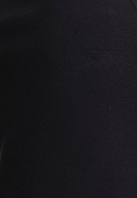 Tecido preto com uma superfície ligeiramente texturizada, exibindo um design suave e estruturado. Apresenta um corte minimalista e sem hardware visível.