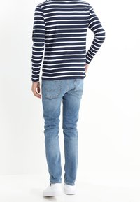 Mörkblå och vit randig långärmad skjorta i kombination med ljusblå jeans och vita sneakers; bilden visar bakifrån av outfiten.