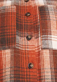 Flanellen overhemd met een ruitpatroon in oranje, bruin en wit, met donkere knopen en een zachte textuur.