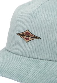 Light blue cordcap med stribet tekstur, flad skygge og et diamantformet broderet logo i mørkerød og guld.