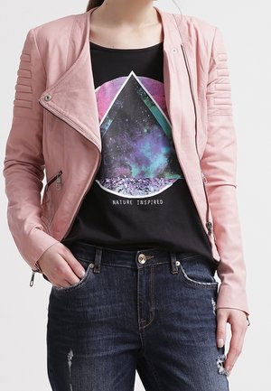 Osoba nosząca różową skórzaną kurtkę na czarnym t-shircie z kolorowym geometrycznym wzorem inspirowanym naturą, połączona z ciemnymi, postarzanymi dżinsami.
