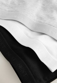 Drei Baumwoll-T-Shirts in Grau, Weiß und Schwarz, die mit elastischen Bändern versehen sind, auf denen der Text "NEXT" eingeprägt ist, in einer Reihe gestapelt.