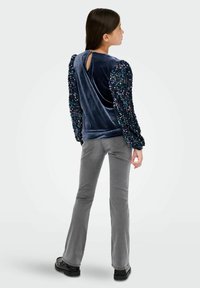 Top de terciopelo azul marino con mangas abullonadas de lentejuelas y abertura en la espalda, combinado con pantalones acampanados grises y zapatos negros.