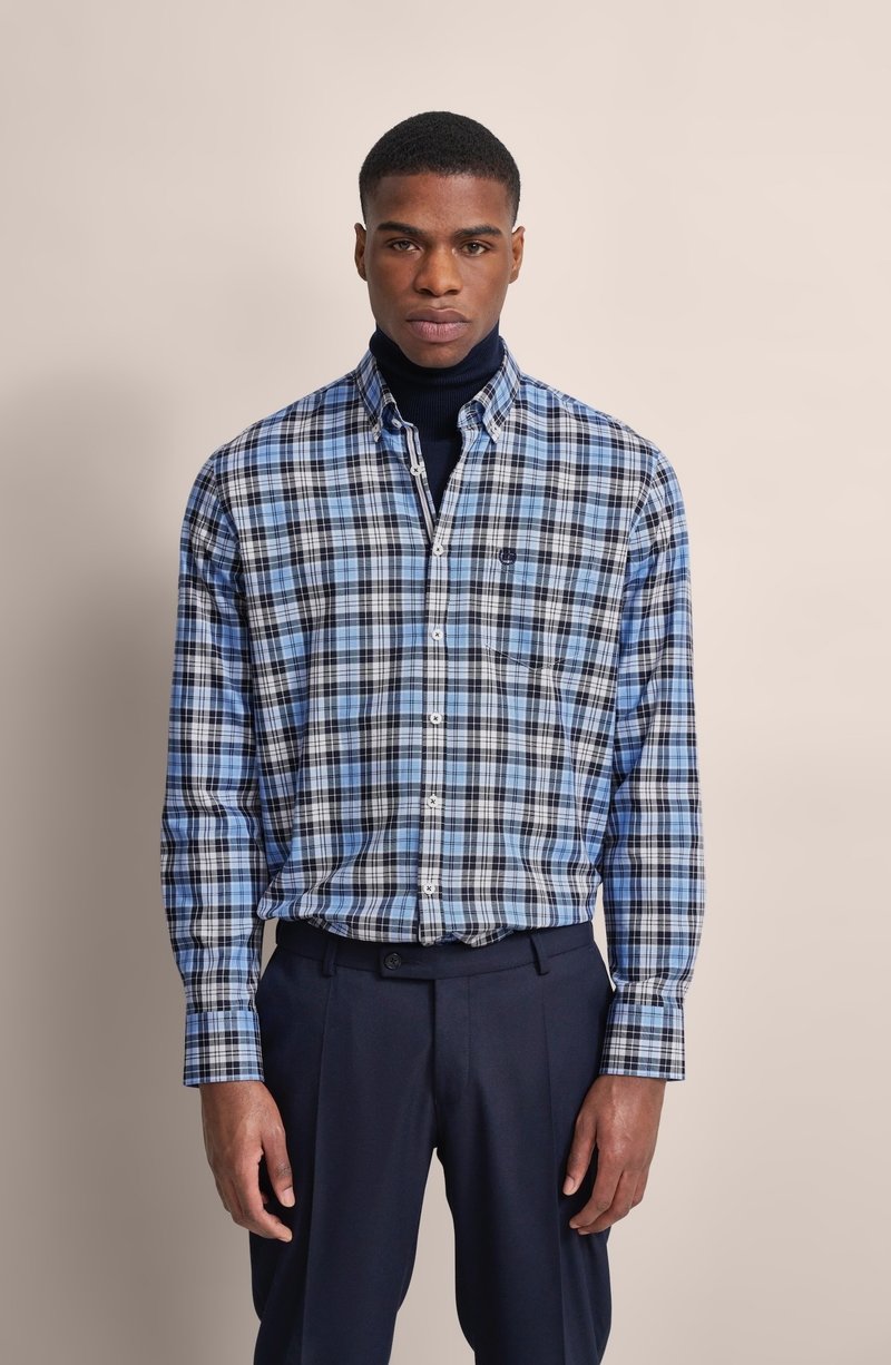 Camicia a quadri blu e nera con colletto, taschino singolo sul petto e polsini abbottonati, abbinata a pantaloni scuri. Tessuto dalla texture liscia.