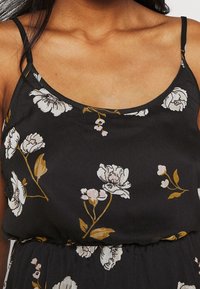 Czarna sukienka z materiału w kwiatowy wzór w bieli i żółci. Posiada cienkie ramiączka i luźny krój, zgromadzona w talii.