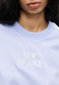 Ανοιχτό μπλε φούτερ με λευκό κεντητό λογότυπο "NEW BALANCE" στο στήθος. Μαλακό ύφασμα, σχέδιο με λαιμόκοψη, διακριτή υφή.